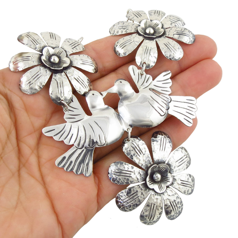 A hand holding a large 925 sterling silver statement necklace featuring two doves and four flower motifs, photographed against a plain white background.