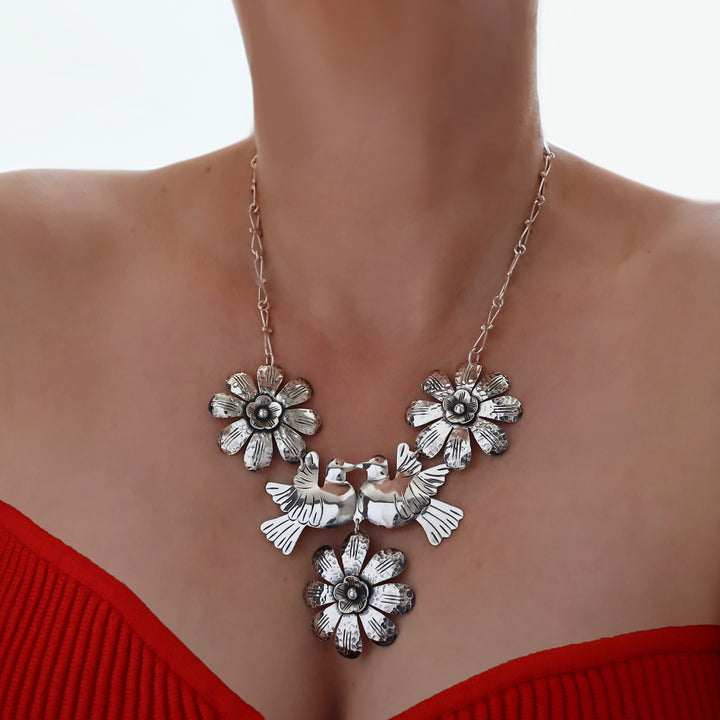 A close-up of a female model wearing a UK hallmarked 925 sterling silver statement necklace featuring two central birds flanked by two flower motifs, styled with a red ribbed top.