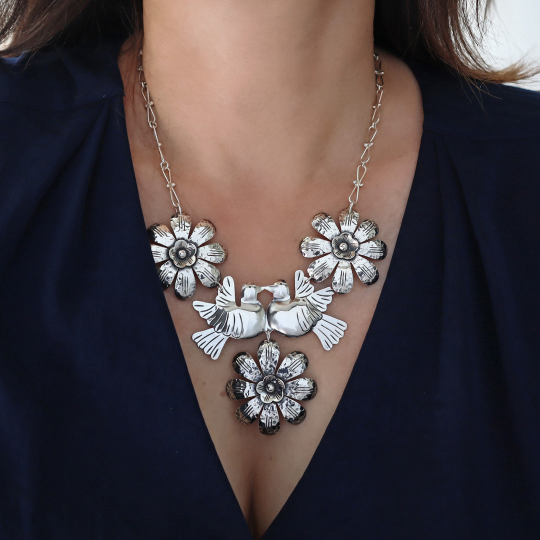 A close-up of a woman wearing a Mexican 925 sterling silver statement necklace with three flower motifs and two central lovebirds, styled with a dark navy blue top.