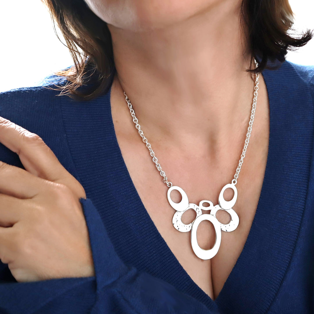 A woman wearing a blue jumper and a large bib style UK 925 sterling silver pendant and chunky chain necklace. 