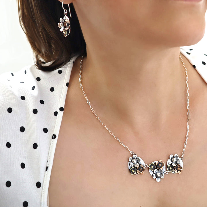 Mixed metal necklace with floral pendants worn by a person against a white background
