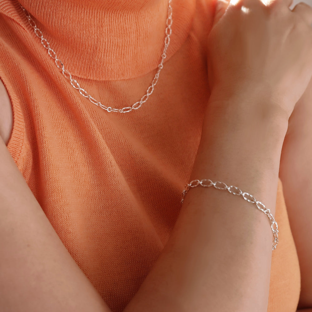 Silver chain bracelet and matching necklace worn by a woman with an orange top. 