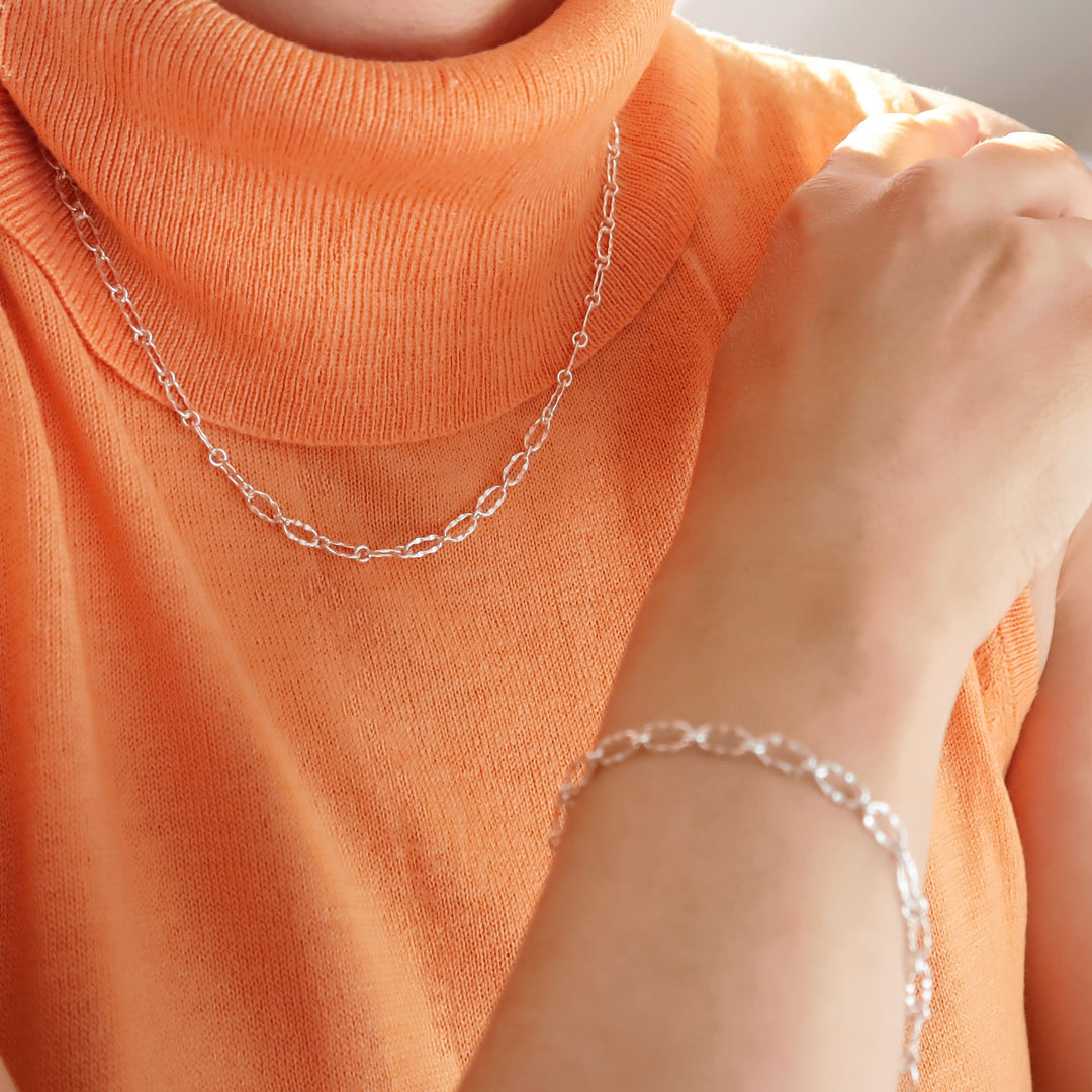 A person in an orange top wearing a hammered link chain necklace and matching bracelet. 