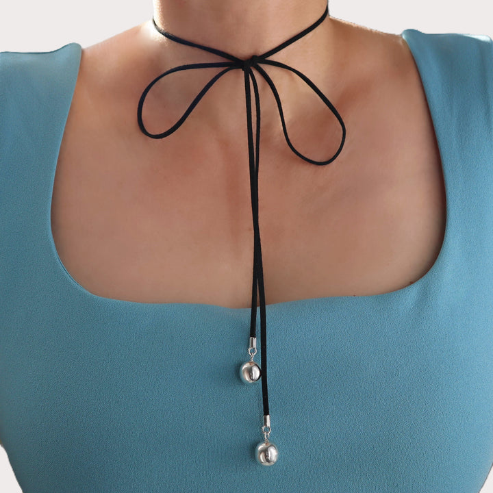 Black choker necklace with silver ball beads on a person wearing a blue top.