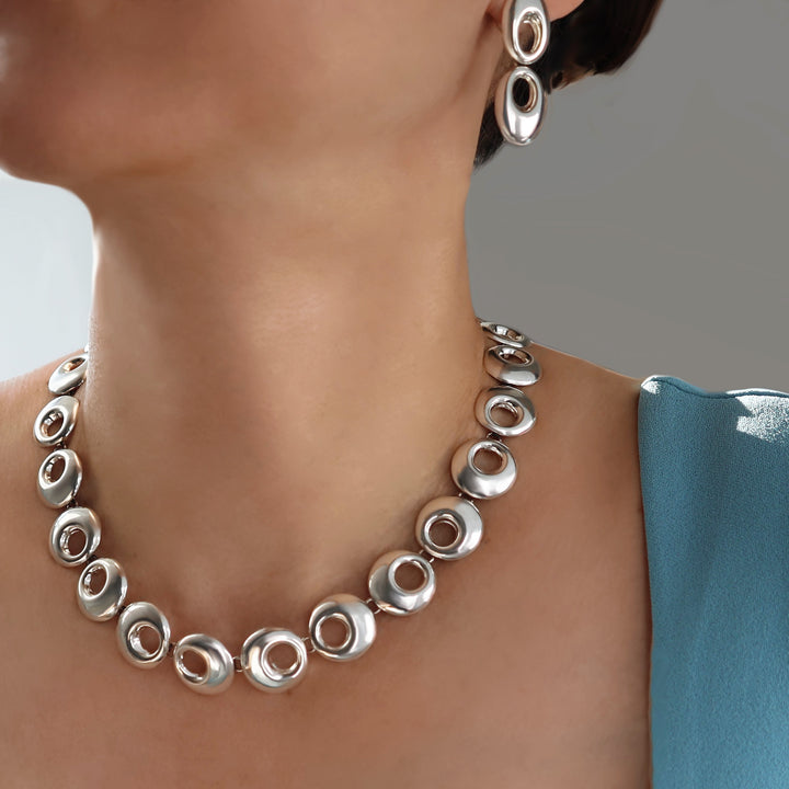 Silver necklace and earrings on a person with a blurred background