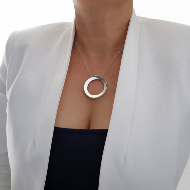 Person wearing a silver necklace with a circular pendant on a white background