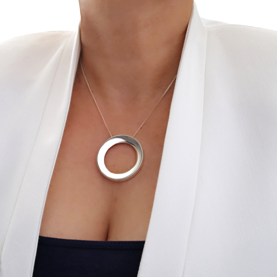 Silver necklace with a circular pendant worn by a person in a white blazer.
