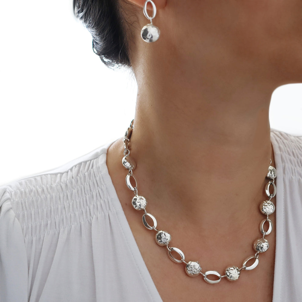 Silver necklace and earrings on a person wearing a white top against a white background