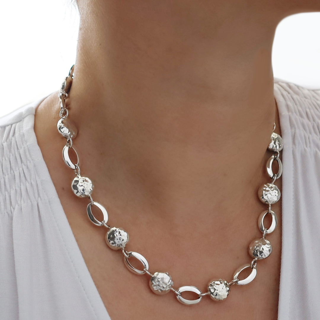Silver necklace with circular and oval links worn by a person against a neutral background