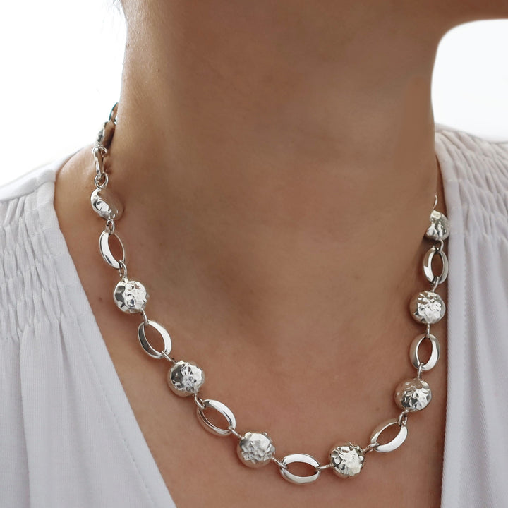 Silver necklace with circular and oval links worn by a person against a neutral background