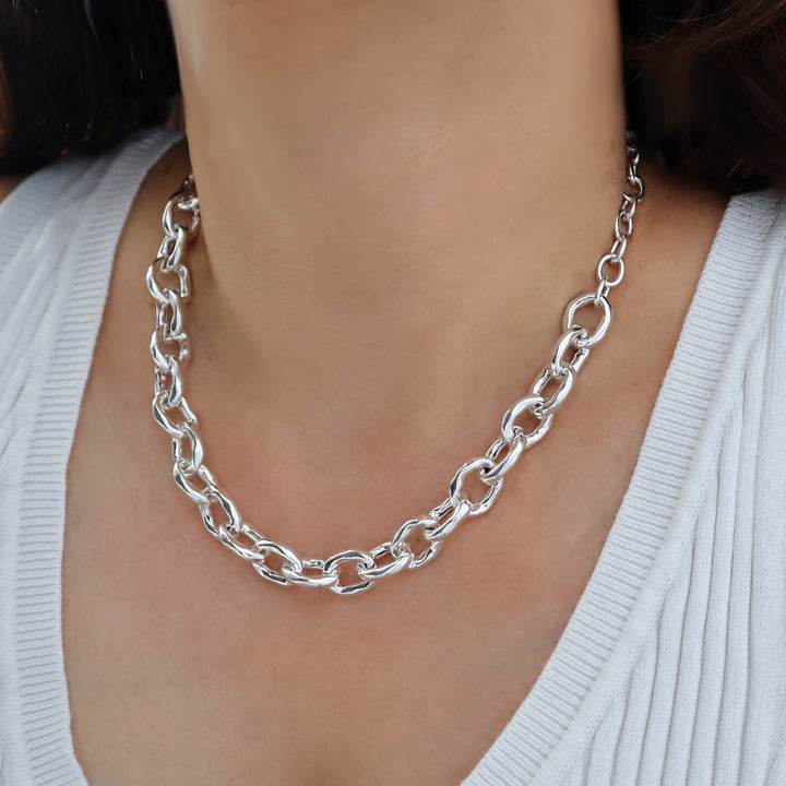 Chunky silver chain necklace worn by a person with a neutral background
