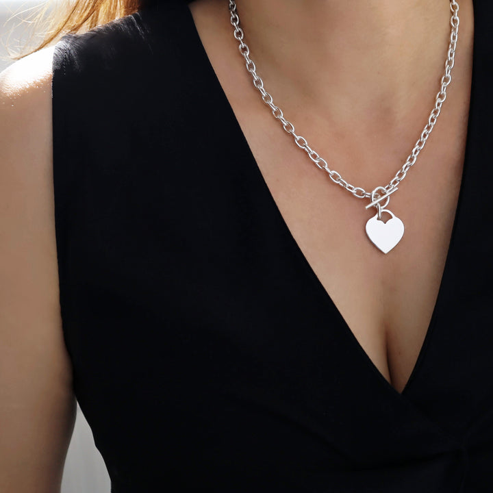 A sterling silver chain necklace with a heart charm worn by a woman with a black blouse