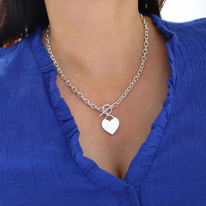 Silver chain necklace with a heart pendant worn by a woman in a blue top.