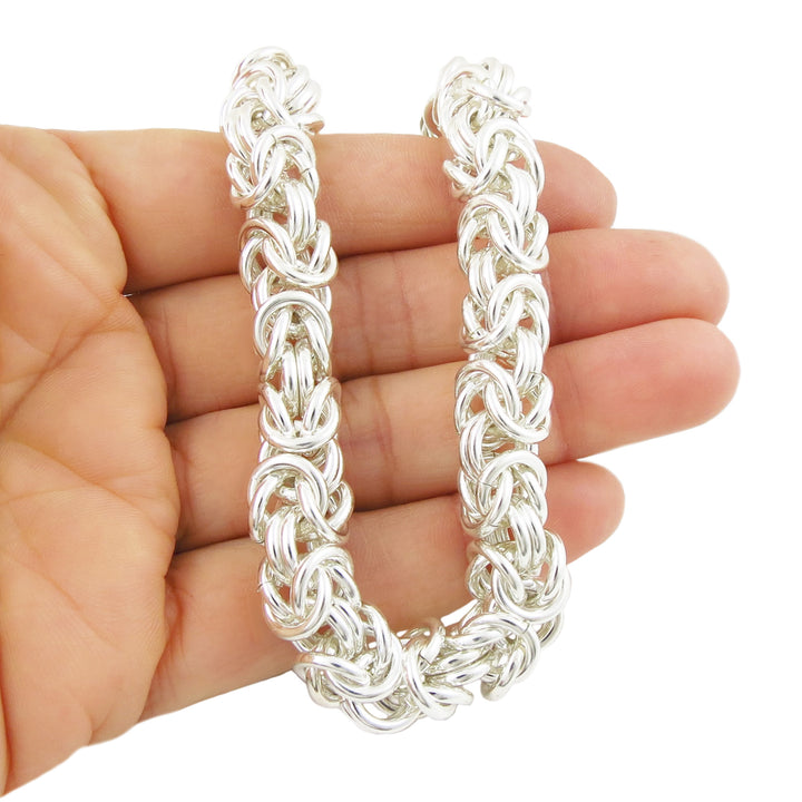 A chunky UK 925 sterling silver byzantine chain necklace held in a person' hand on a white background. 