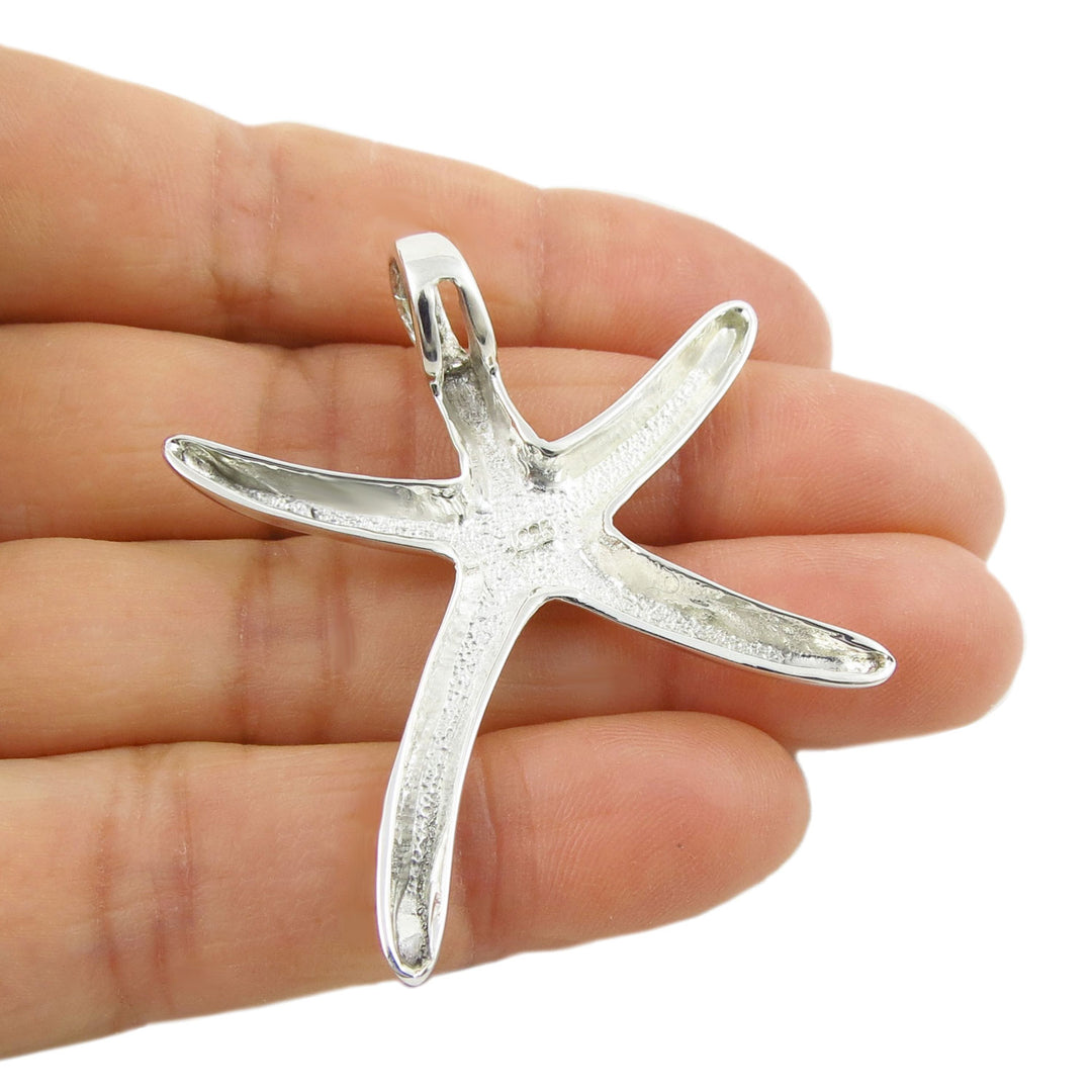 Large sterling 925 silver starfish pendant held upside down between fingers to show the large integrated bail on a white background