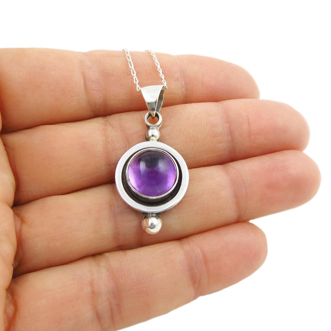 Silver pendant with a purple amethyst gemstone held in a hand on a white background