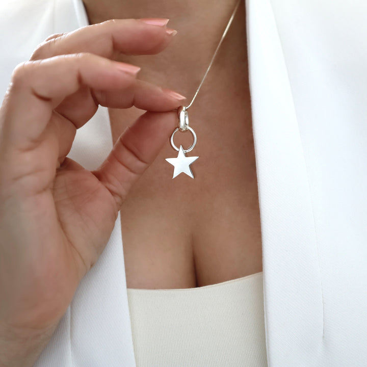 Silver necklace with a star pendant held by a hand against a white background