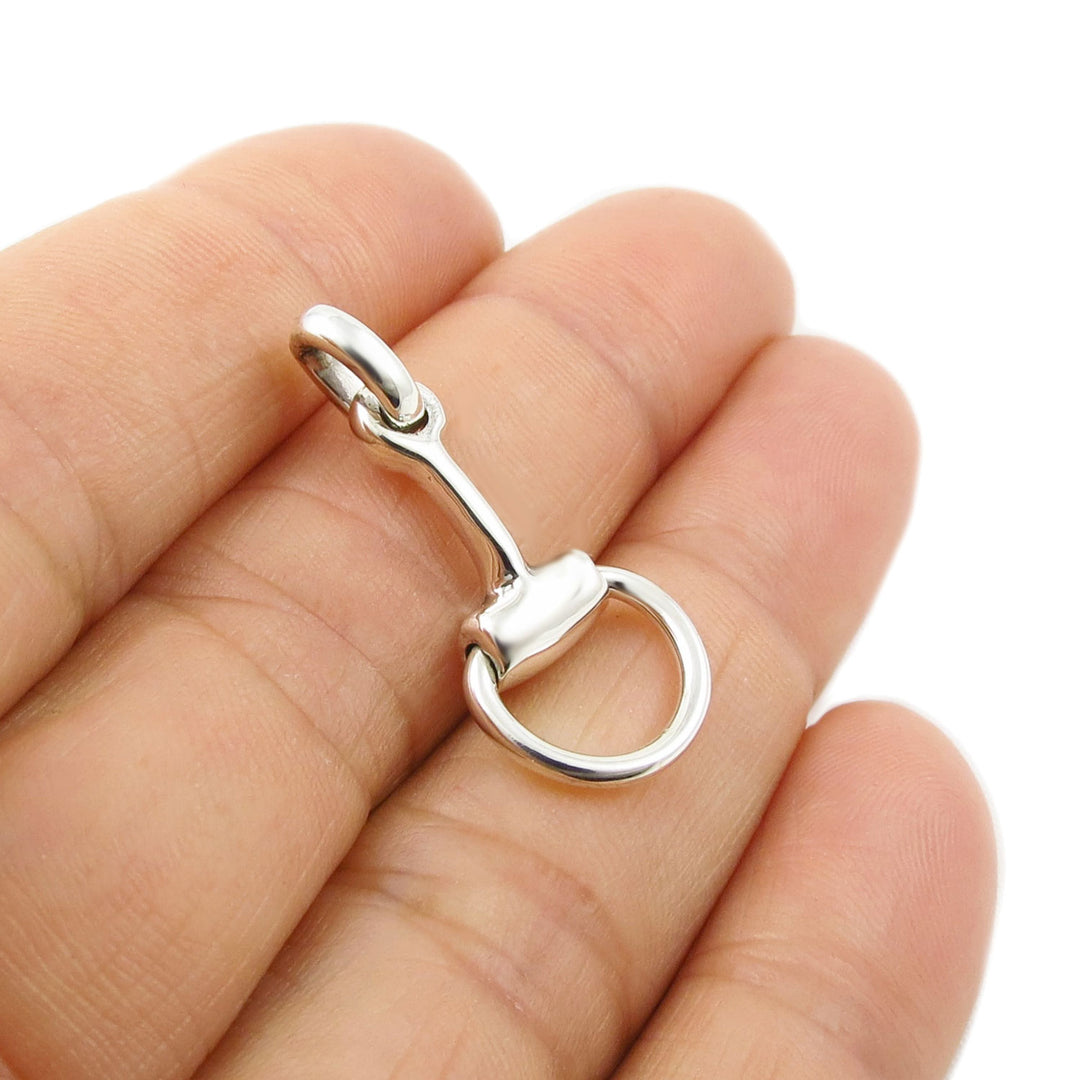 Equestrian sterling Silver horse snaffle bit pendant ladies jewellery held between fingers on a white background