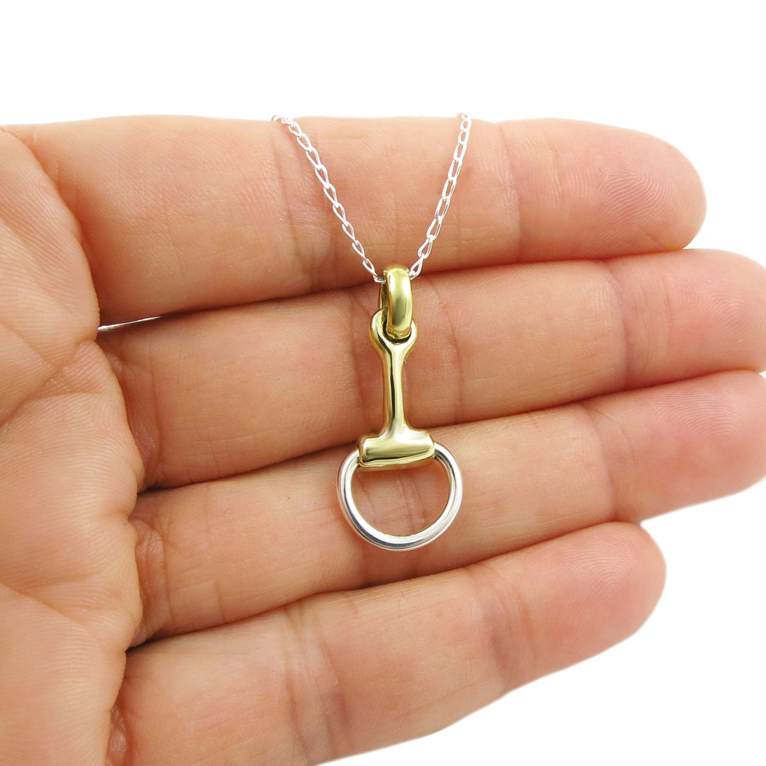 Gold and 925 silver horse snaffle bit pendant on a curb chain held in a hand against a white background