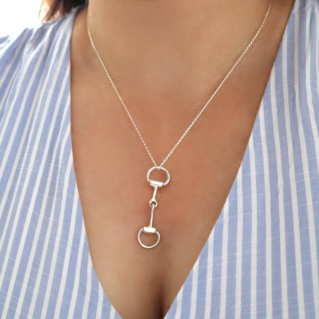 Silver necklace with a unique snaffle bit pendant worn by a person against a striped background