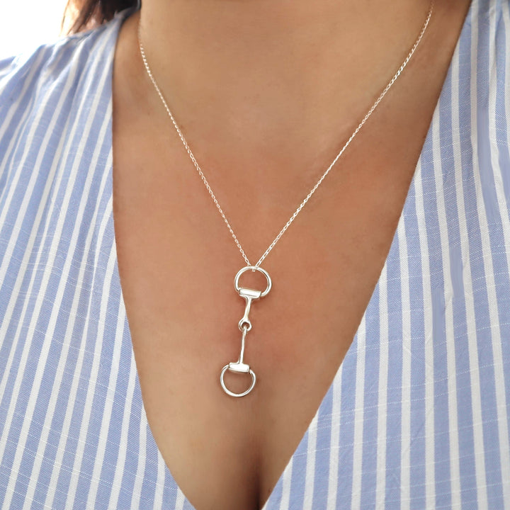 Silver necklace with a unique snaffle bit pendant worn by a person against a striped background