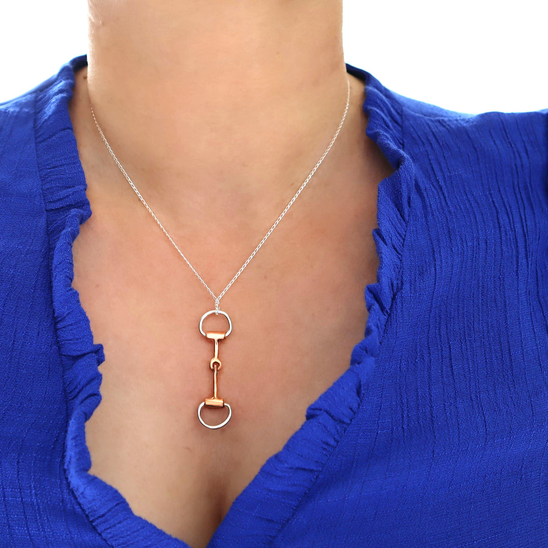Necklace with a unique two tone horsebit snaffle pendant worn by a person in a blue top