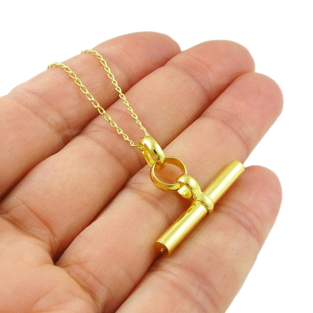 A bright yellow gold large t-bar pendant and curb chain necklace held in a persons hand on a whte background