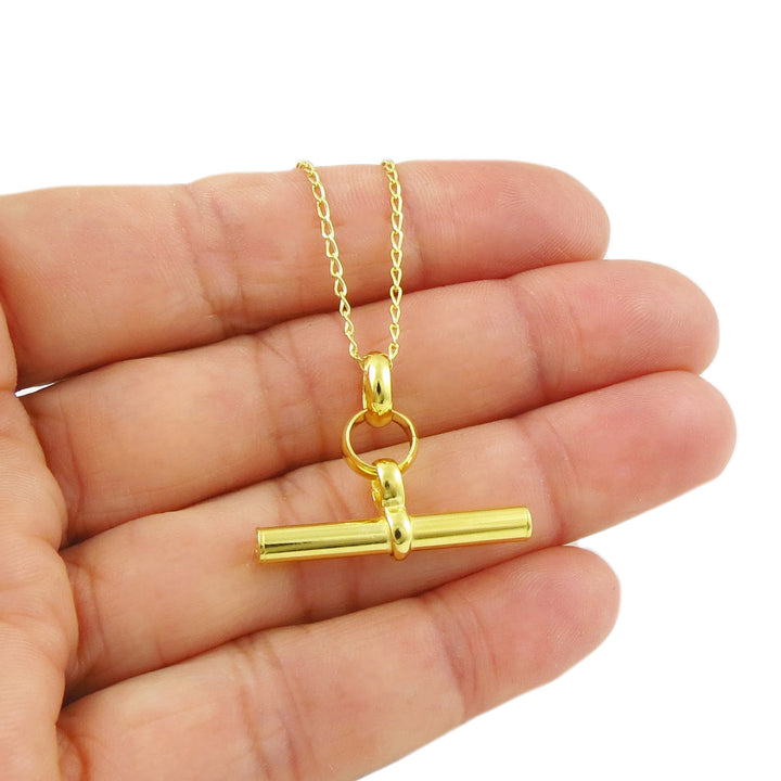 A large yellow gold t-bar pendant chain necklace held in a person's hand