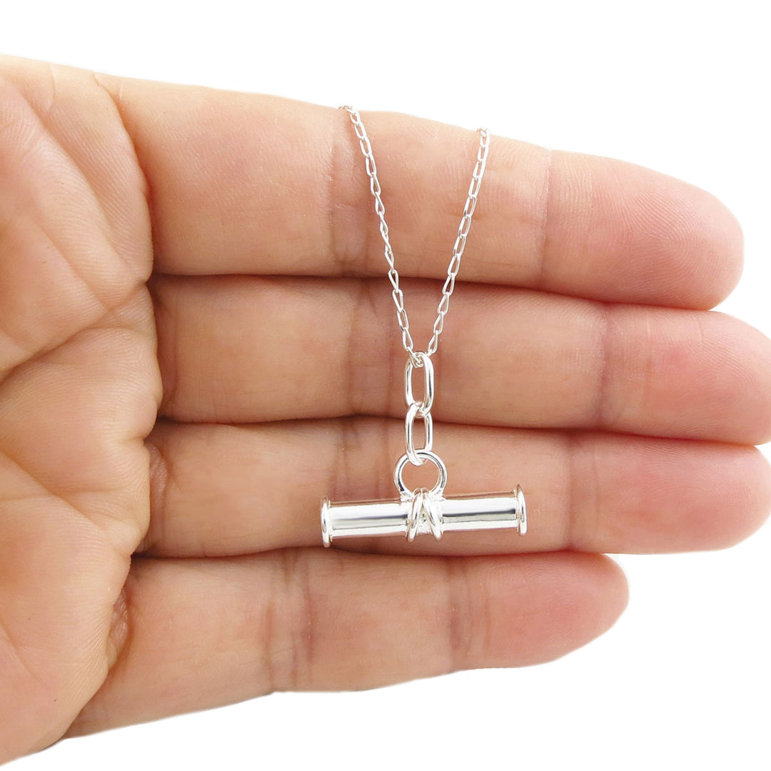 Sterling 925 Silver necklace with a cylindrical t-bar pendant on a curb chain held in a hand on a white background