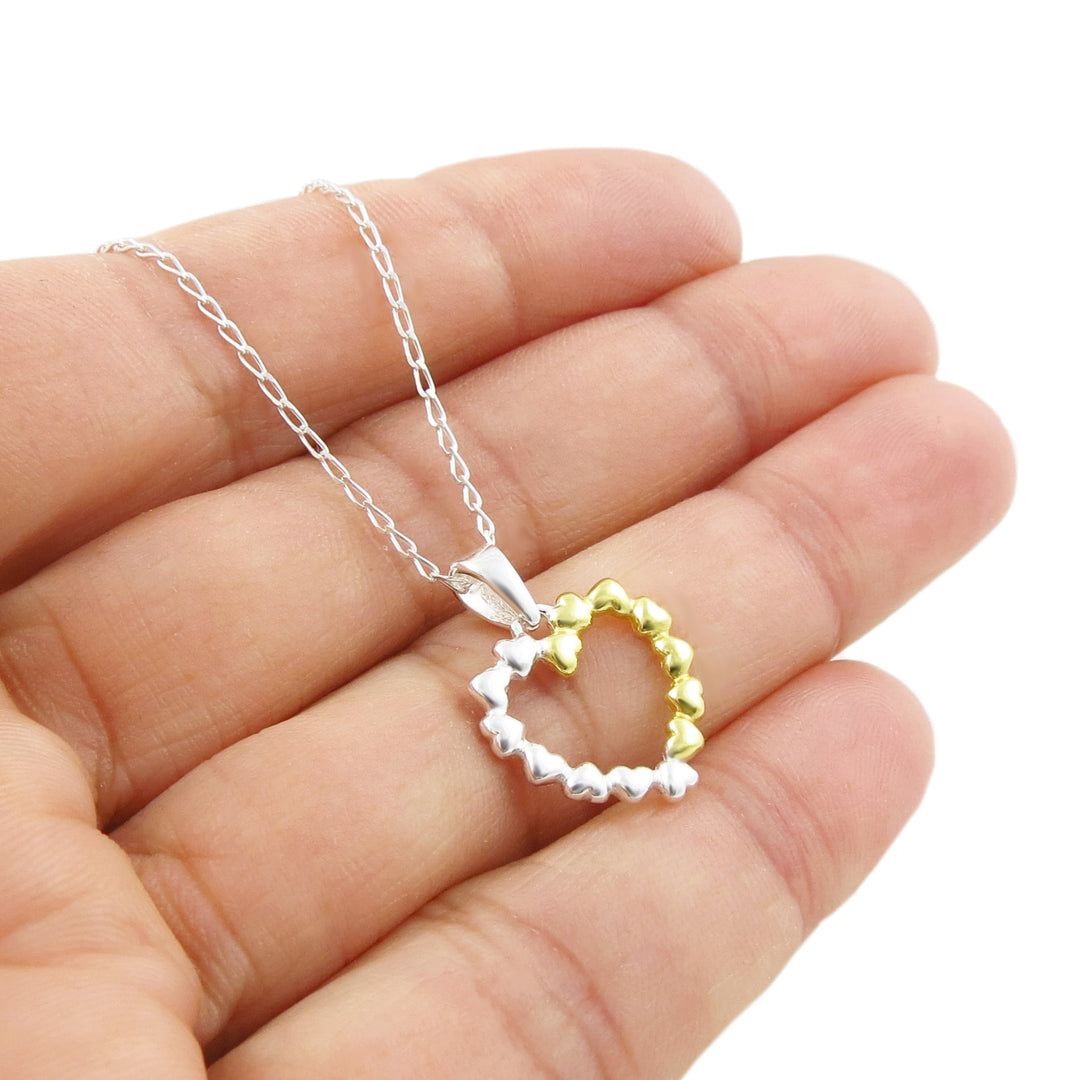 Gold and 925 sterling silver heart-shaped pendant on a 925 silver chain held between fingers against a white background