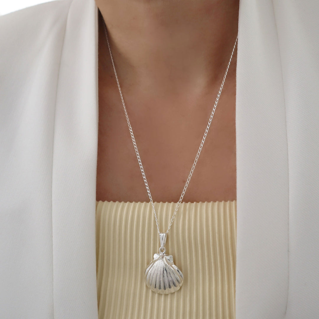 Sterling 925 Silver necklace with a sea shell pendant and chain worn by a woman in a light-colored outfit.