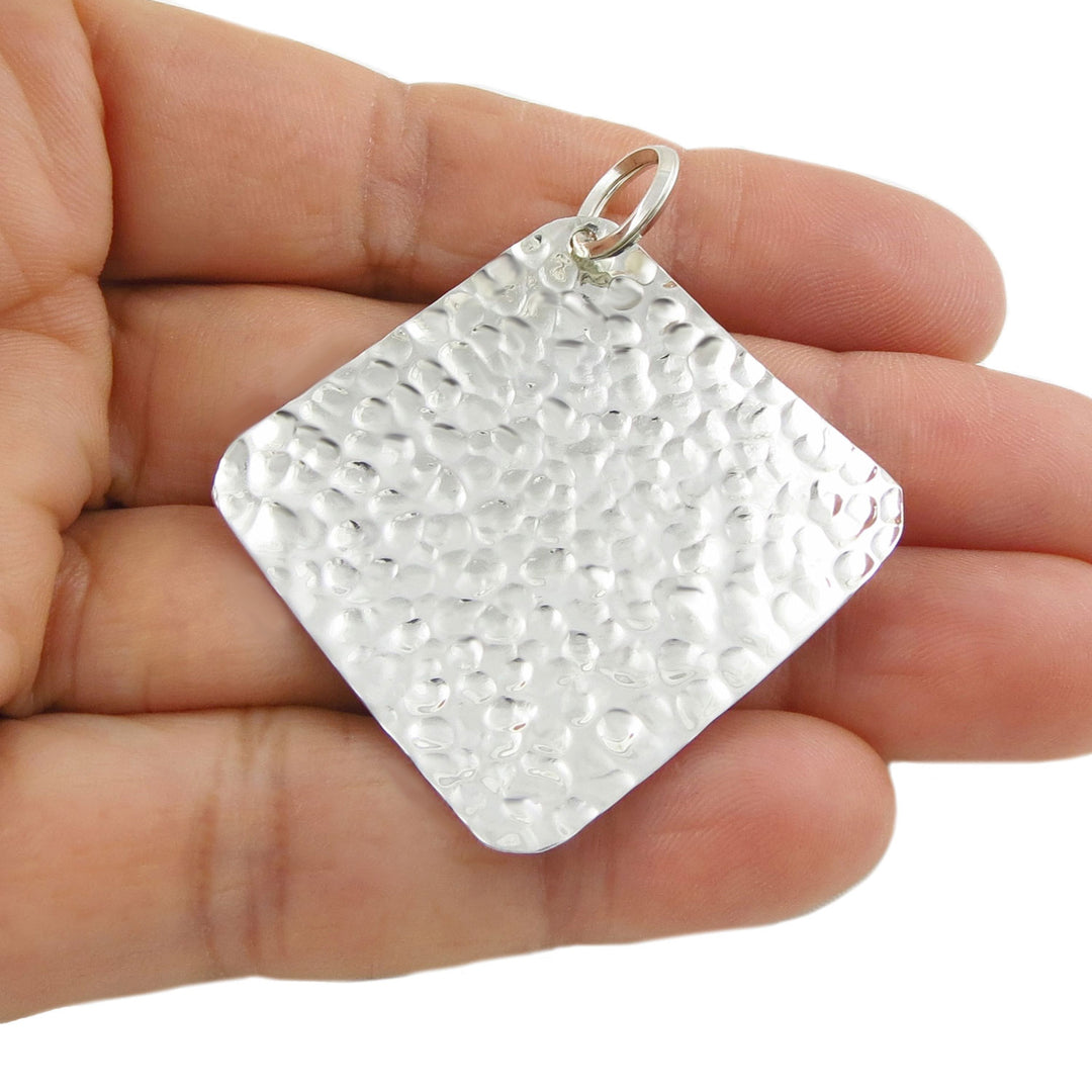 A large modern 925 sterling silver hammered square pendant ladies jewellery held in a hand against a white background