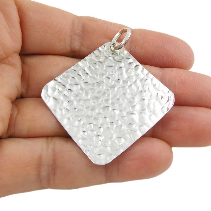 A large modern 925 sterling silver hammered square pendant ladies jewellery held in a hand against a white background