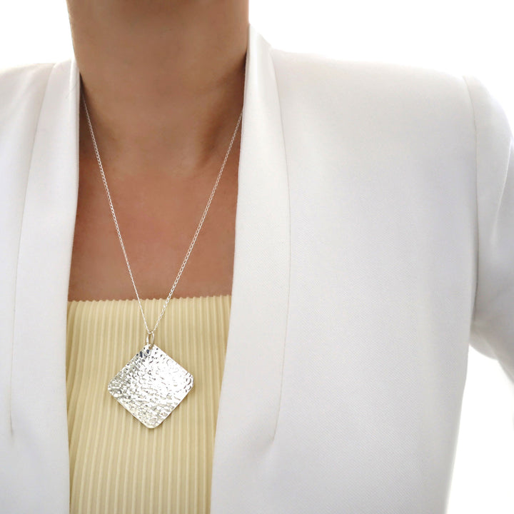 Large 925 sterling silver hammered pendant and long dangling curb chain necklace worn by a female in a white outfit.