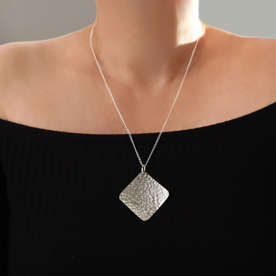 Large modern square hammered pendant and chain 925 silver necklace on a woman wearing a black top.