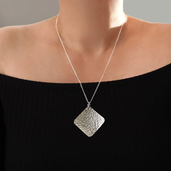 Large modern square hammered pendant and chain 925 silver necklace on a woman wearing a black top.