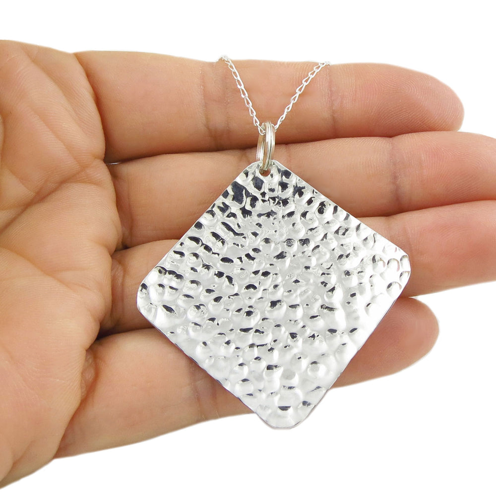 925 sterling silver textured hammered square pendant necklace on a curb chain held in a ladies hand against a white background