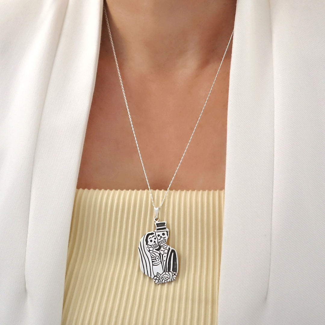 Sterling 925 Silver day of the dead bride and groom pendant and chain necklace worn by a woman in a white outfit. 