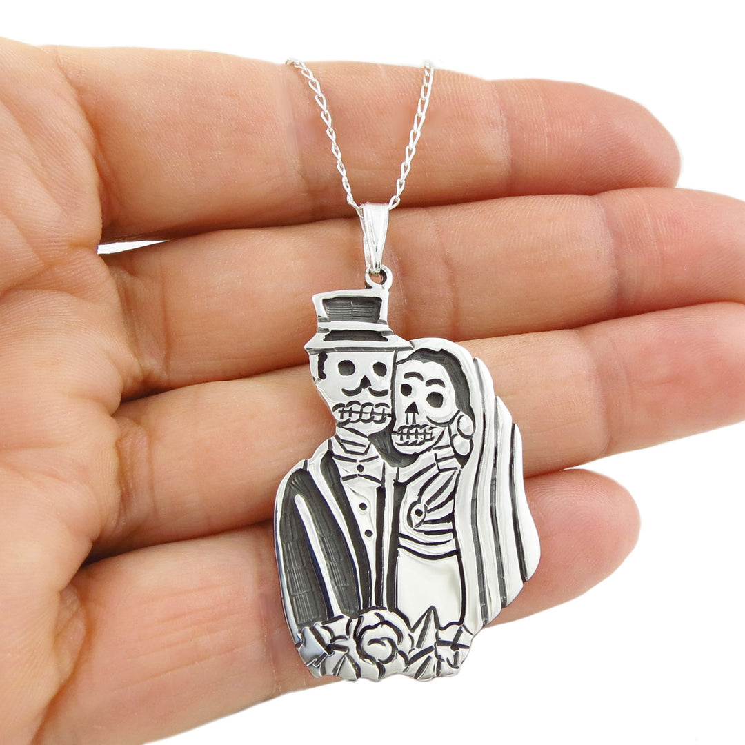 Sterling 925 silver day of the dead bride and groom pendant on a curb chain held in a woman's hand against a white background