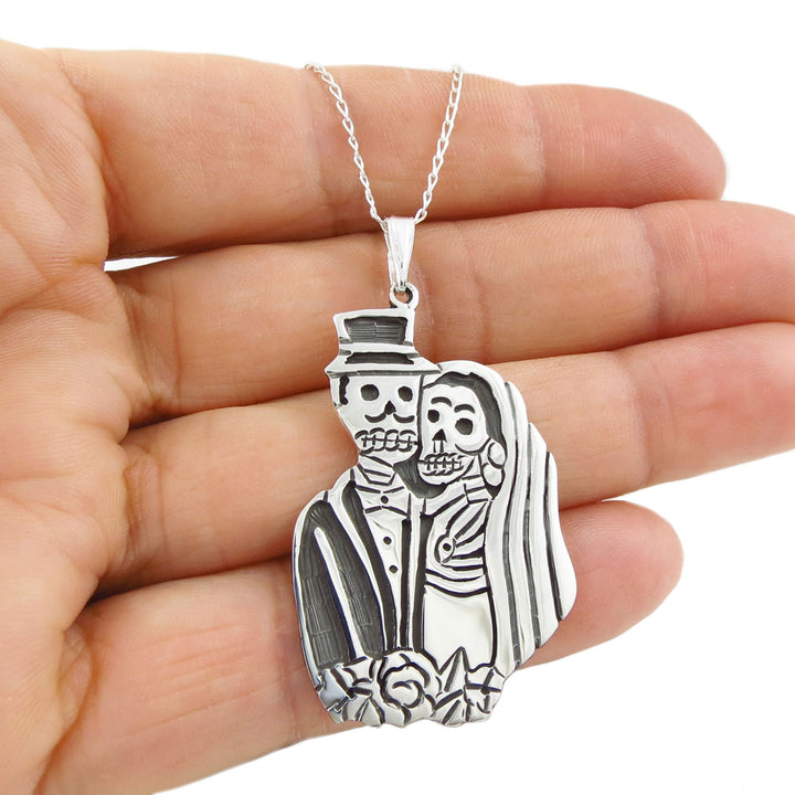 Sterling 925 silver day of the dead bride and groom pendant on a curb chain held in a woman's hand against a white background