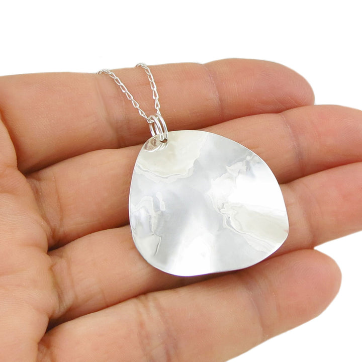 Woman's hand holding a 925 sterling silver necklace with a large, round hammered pendant on a white background