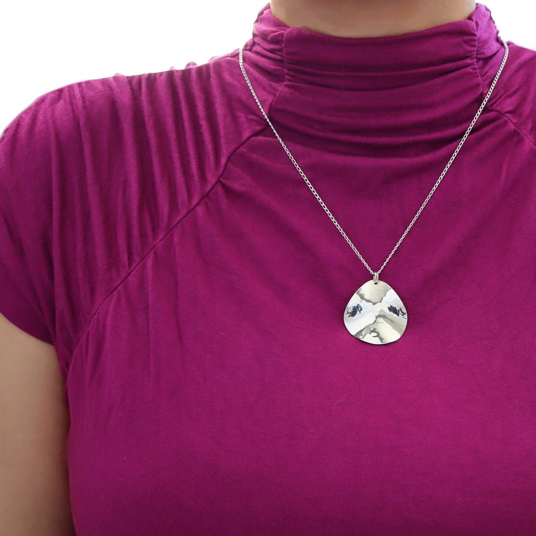 A llarge 925 sterling silver sculpted pendant and curb chain necklace on a woman wearing a purple shirt