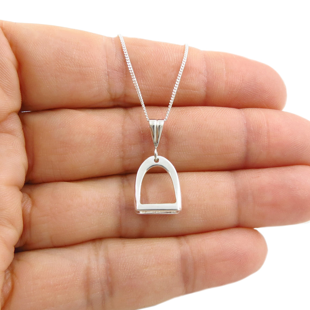 Solid 925 sterling silver equestrian horse stirrup pendant and trace chain necklace held in a person's hand on a plain background. 