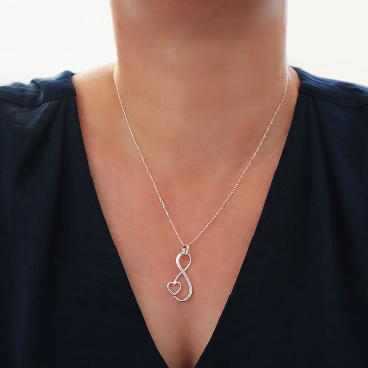 Sterling 925 Silver eternity figure of eight necklace with a heart-shape worn by a woman in a dark blue top.