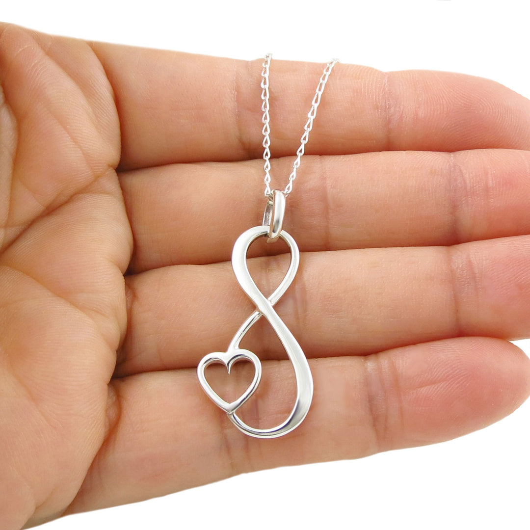 925 silver necklace with an infinity figure of eight and love heart symbol held in a woman's hand.