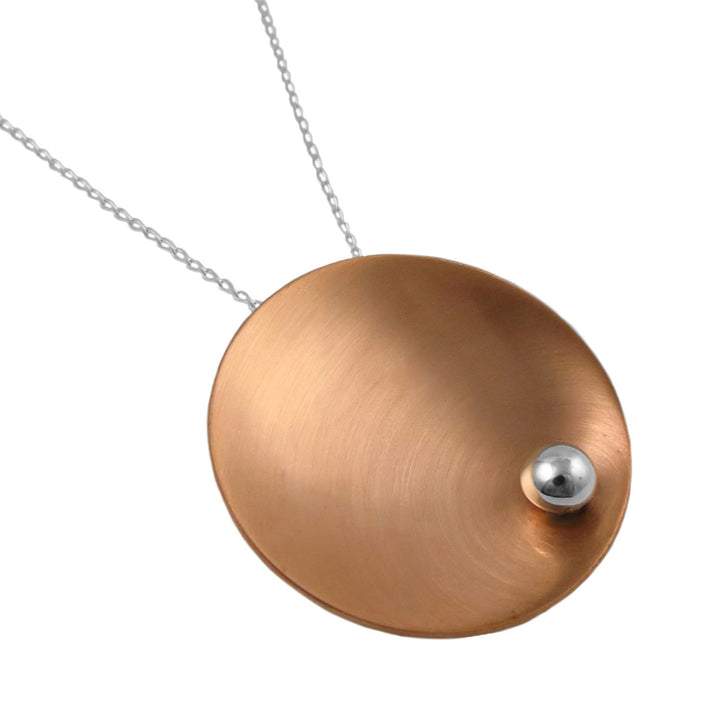 A large brushed copper pendant necklace with a small silver sphere on a white background