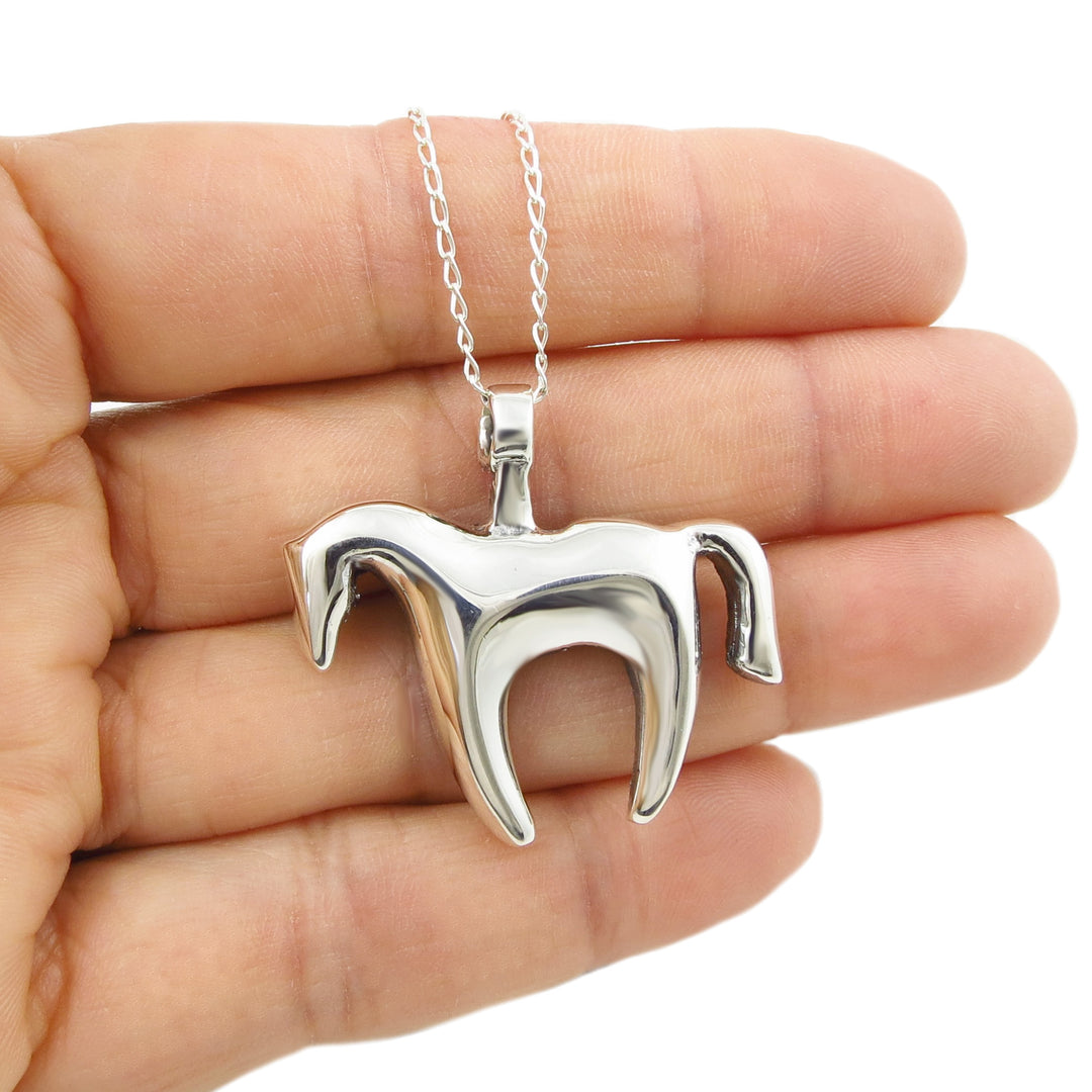 Silver horse-shaped pendant on a chain held in a hand against a white background