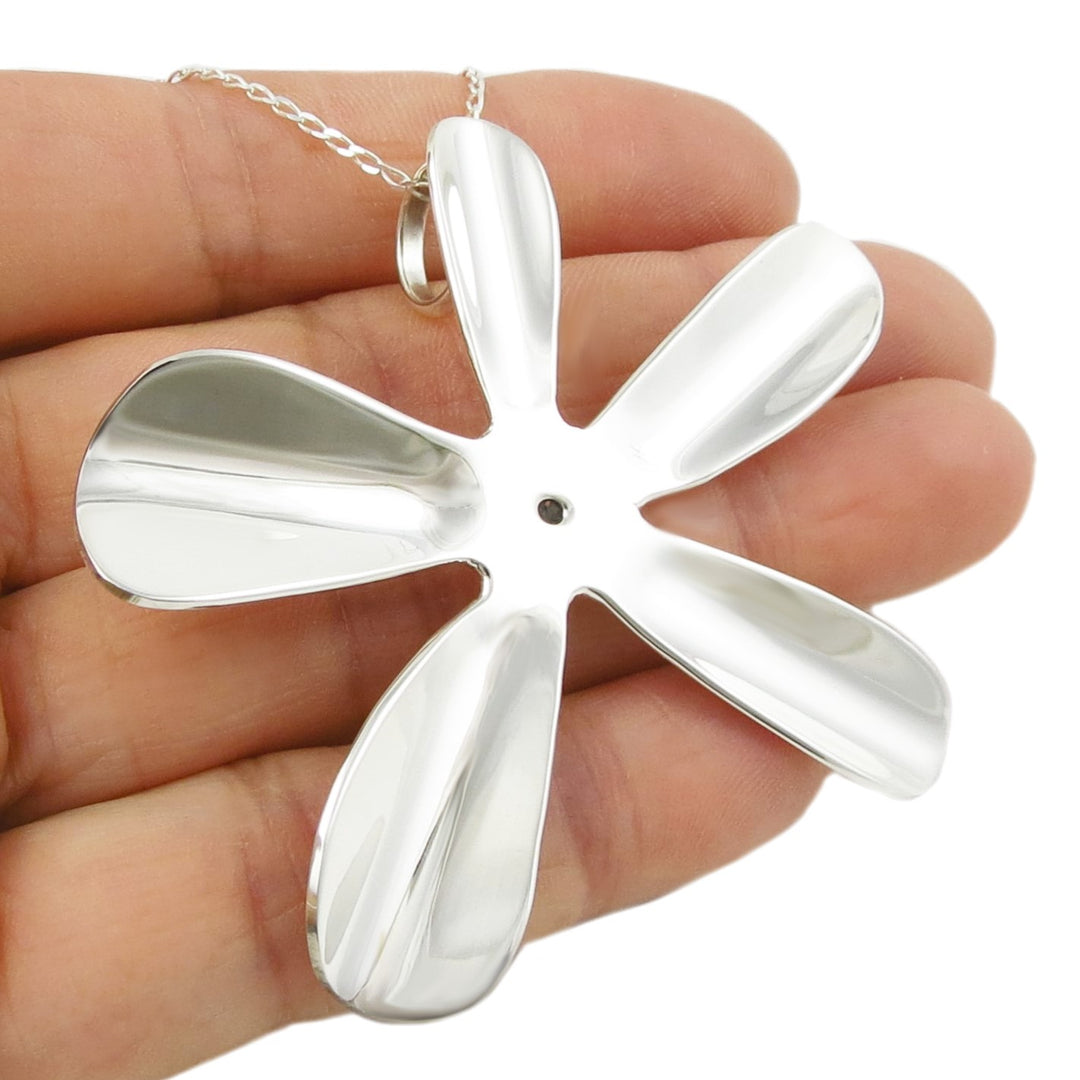Silver flower-shaped daisy pendant held between fingers against a white background
