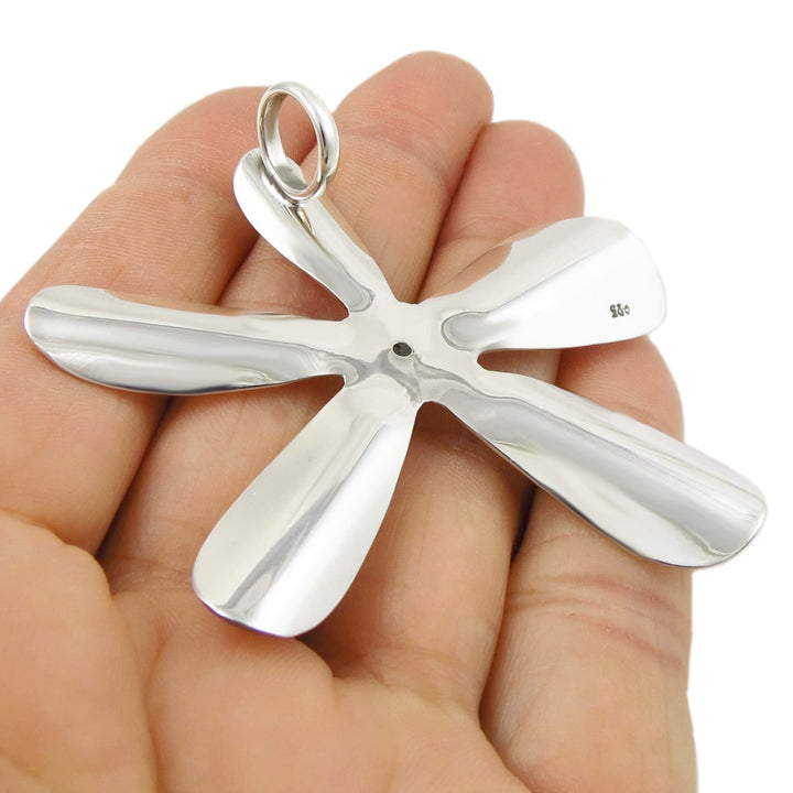 Silver flower-shaped pendant held in a hand against a white background