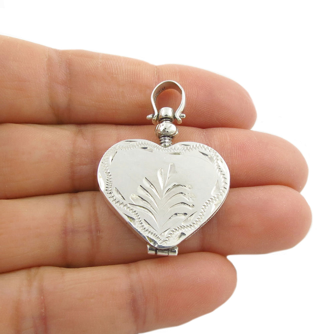 925 silver heart-shaped locket style pendant jewellery for women held between fingers on a white background